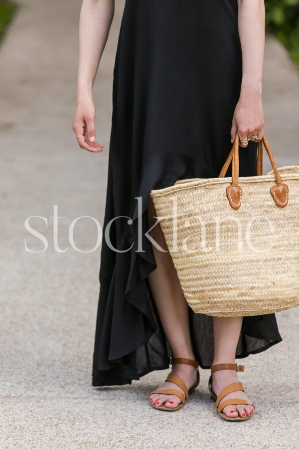 Vertical stock photo of a woman wearing a black summer dress holding a French market basket.