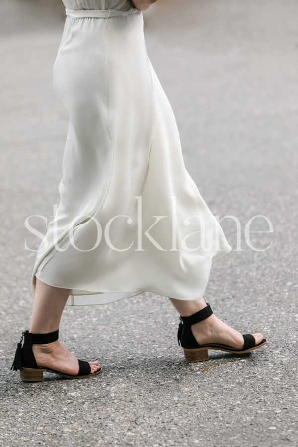 Vertical stock photo of a woman in a white dress walking in the street.