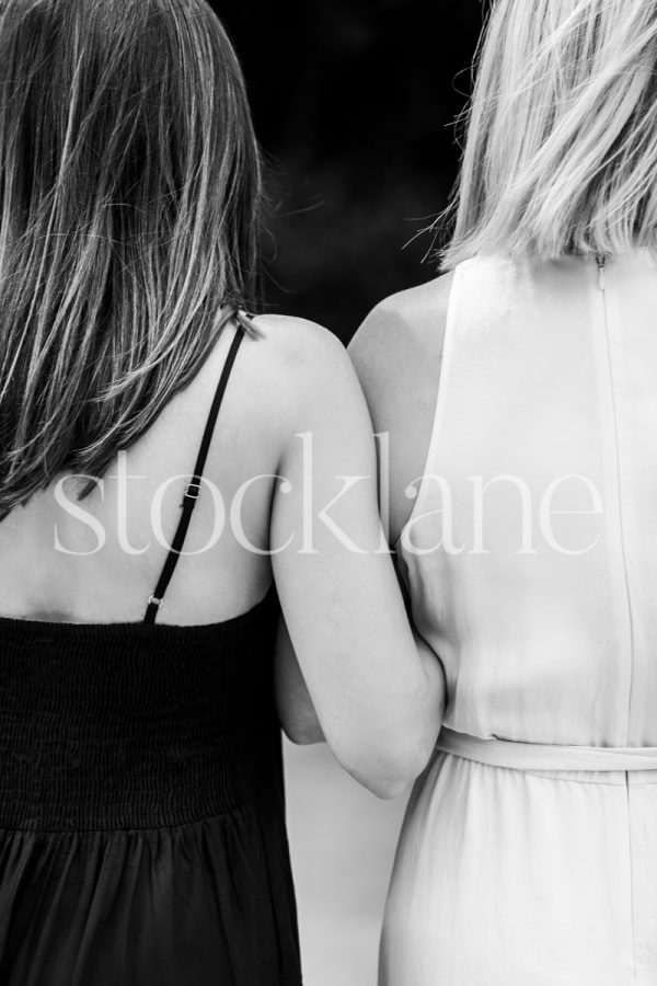 Vertical black and white photo of two women interlocking arms.