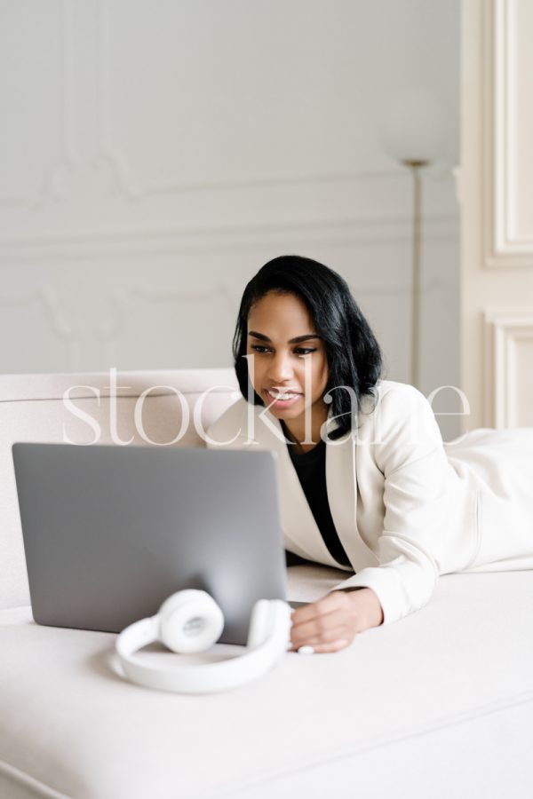 Vertical stock photo of a woman wearing a white suit, working on a laptop computer.