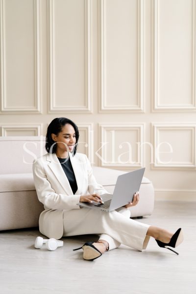 Vertical stock photo of a woman wearing a white suit, working on a laptop computer.