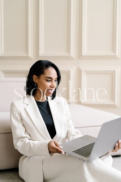 Vertical stock photo of a woman wearing a white suit, working on a laptop computer.