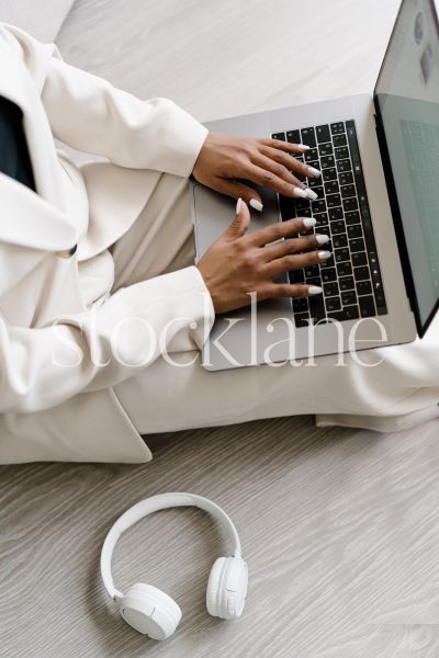 Vertical stock photo of a woman wearing a white suit, working on a laptop computer.