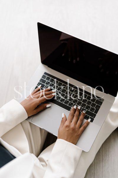 Vertical stock photo of a woman wearing a white suit, working on a laptop computer.