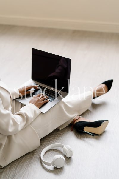 Vertical stock photo of a woman wearing a white suit, working on a laptop computer.