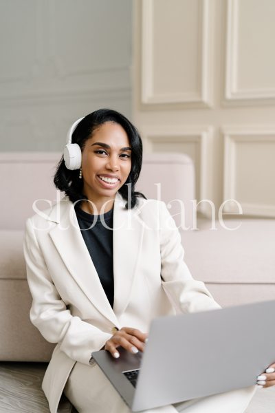 Vertical stock photo of a woman wearing a white suit, working on a laptop computer.