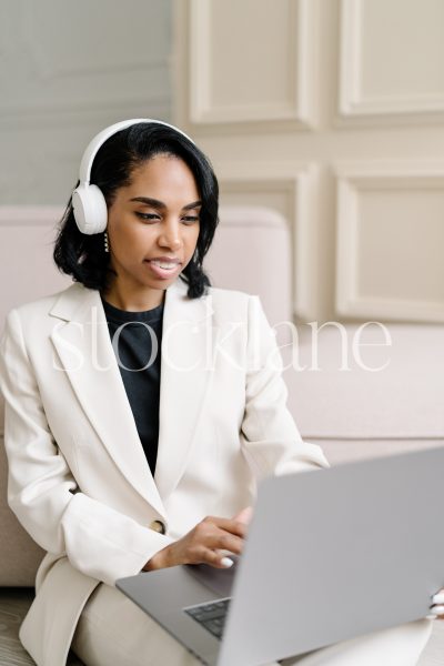 Vertical stock photo of a woman wearing a white suit, working on a laptop computer.