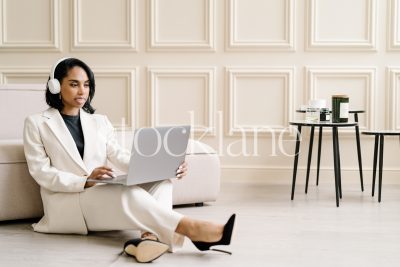 Horizontal stock photo of a woman wearing a white suit, working on a laptop computer.