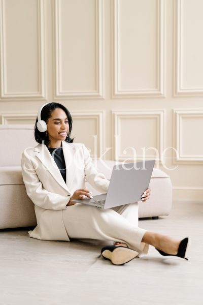 Vertical stock photo of a woman wearing a white suit, working on a laptop computer.