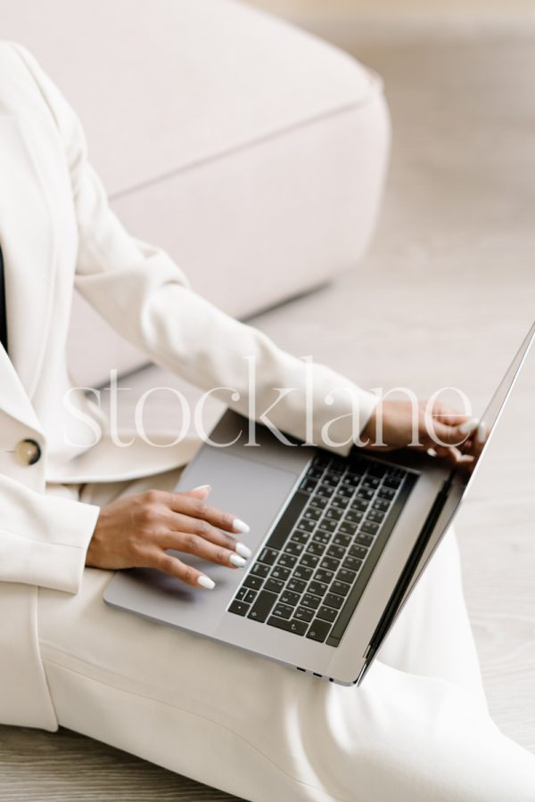 Vertical stock photo of a woman wearing a white suit, working on a laptop computer.