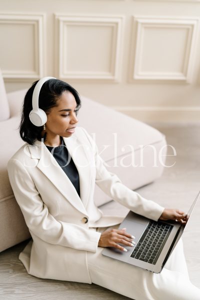 Vertical stock photo of a woman wearing a white suit, working on a laptop computer.