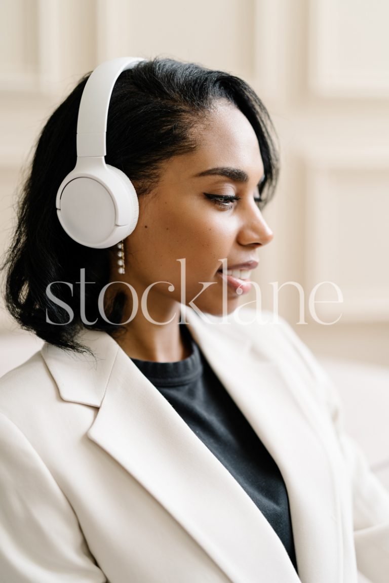 Vertical stock photo of a woman wearing a white suit, with headphones on.