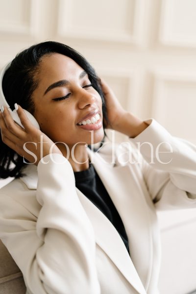 Vertical stock photo of a woman wearing a white suit, listening to music with headphones.