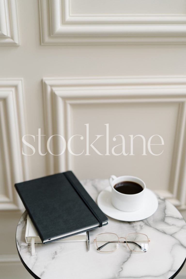 Vertical stock photo of a marble-top table with a cup of coffee and a black notebook.