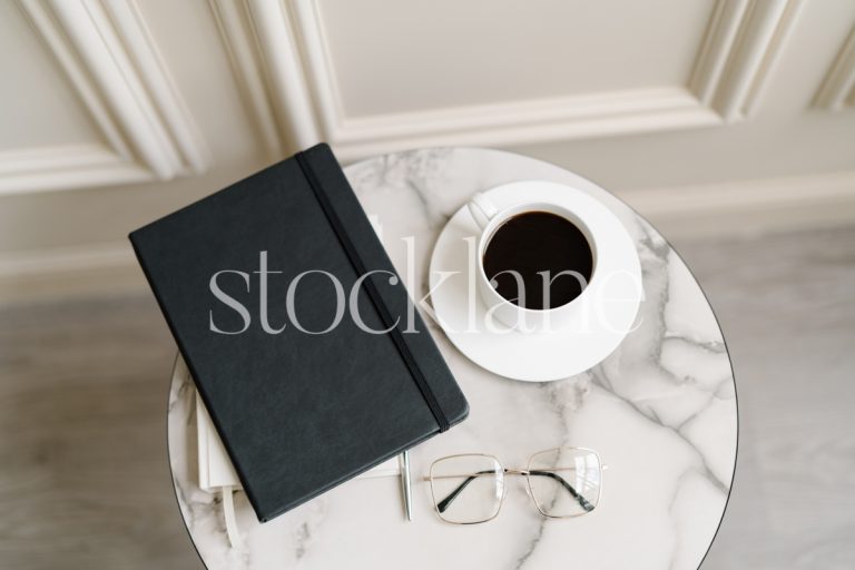 Horizontal stock photo of a marble-top table with a cup of coffee and a black notebook.