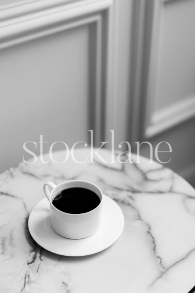 Vertical black and white stock photo of a marble-top table with a cup of coffee.