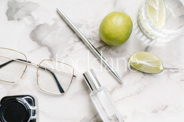 Horizontal stock photo of a marble top table with limes, water, glasses and other personal items.