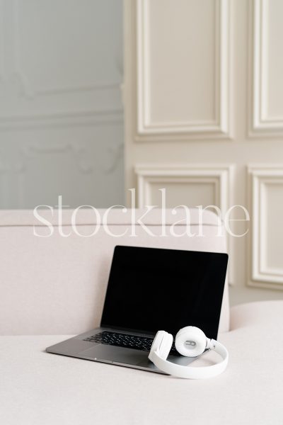 Vertical stock photo of a laptop and headphones on a blush pink couch.