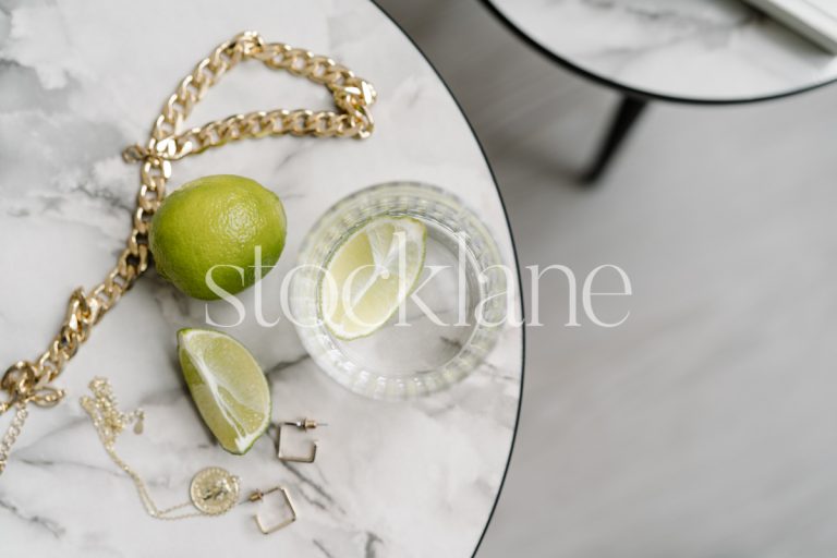 Horizontal stock photo of a marble-top table with water, limes and jewelry.