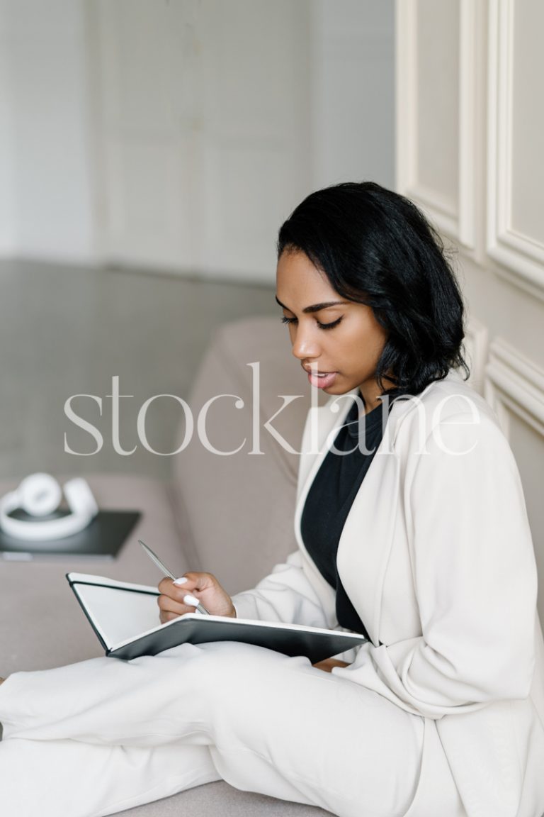 Vertical stock photo of a woman writing on a black notebook.