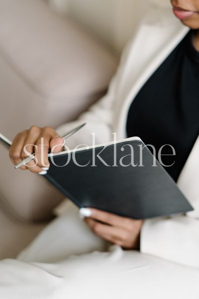 Vertical stock photo of a woman writing on a black notebook.