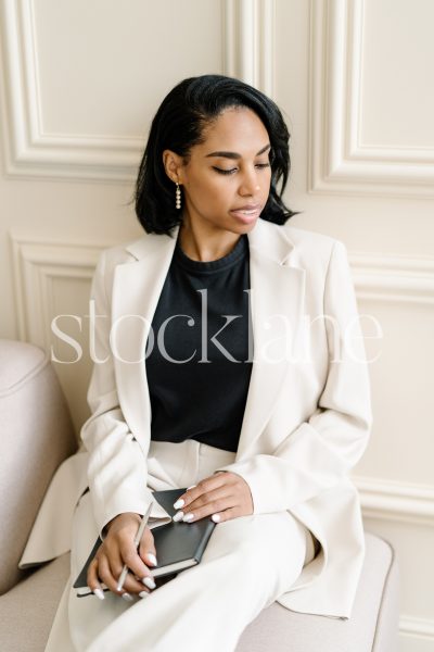 Vertical stock photo of a woman writing on a black notebook.