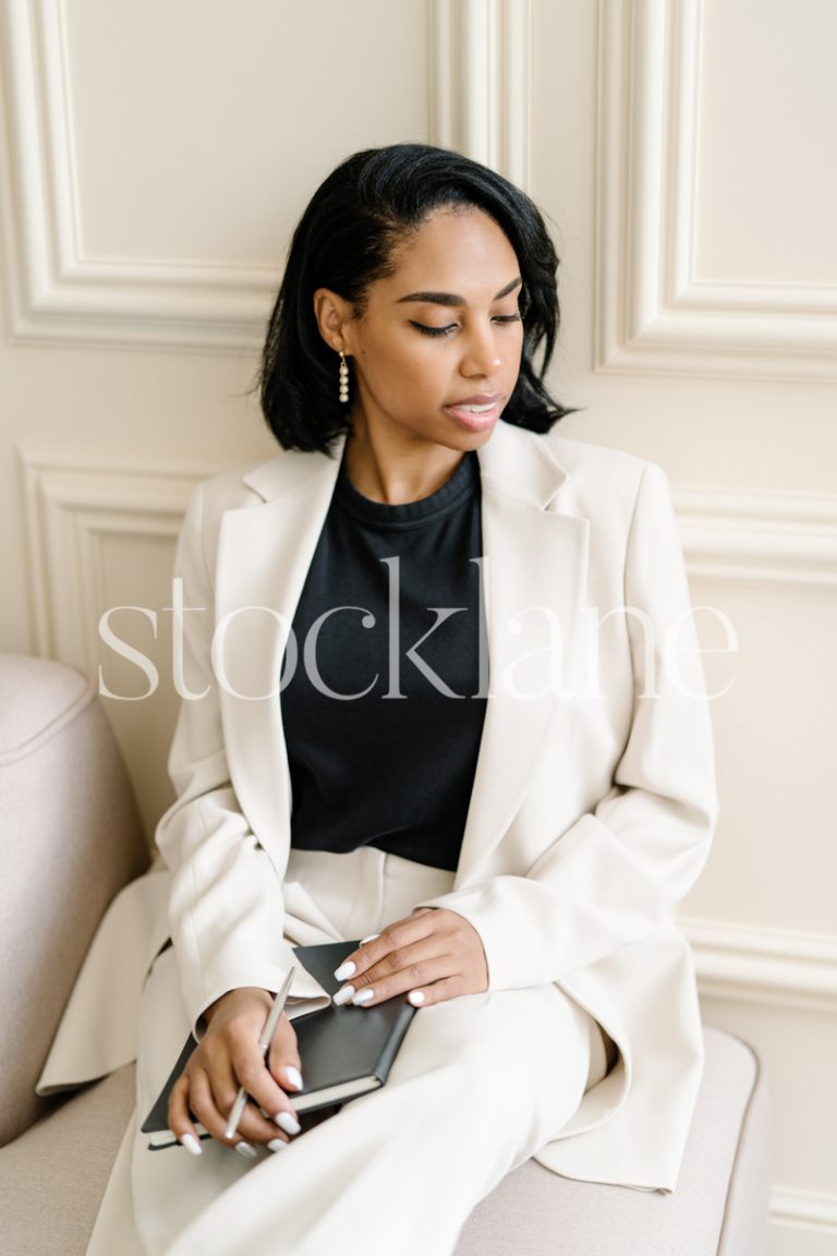 Vertical stock photo of a woman writing on a black notebook.