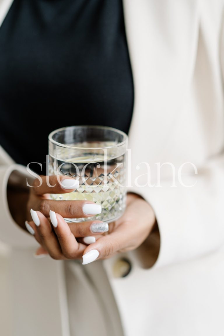 Vertical stock photo of a woman in a white suit holding a glass of water.