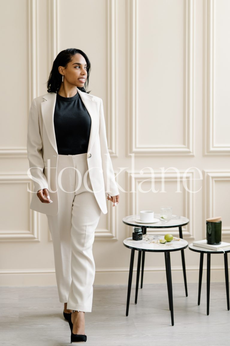 Vertical stock photo of a woman wearing a white suit, in a neutral-colored room.