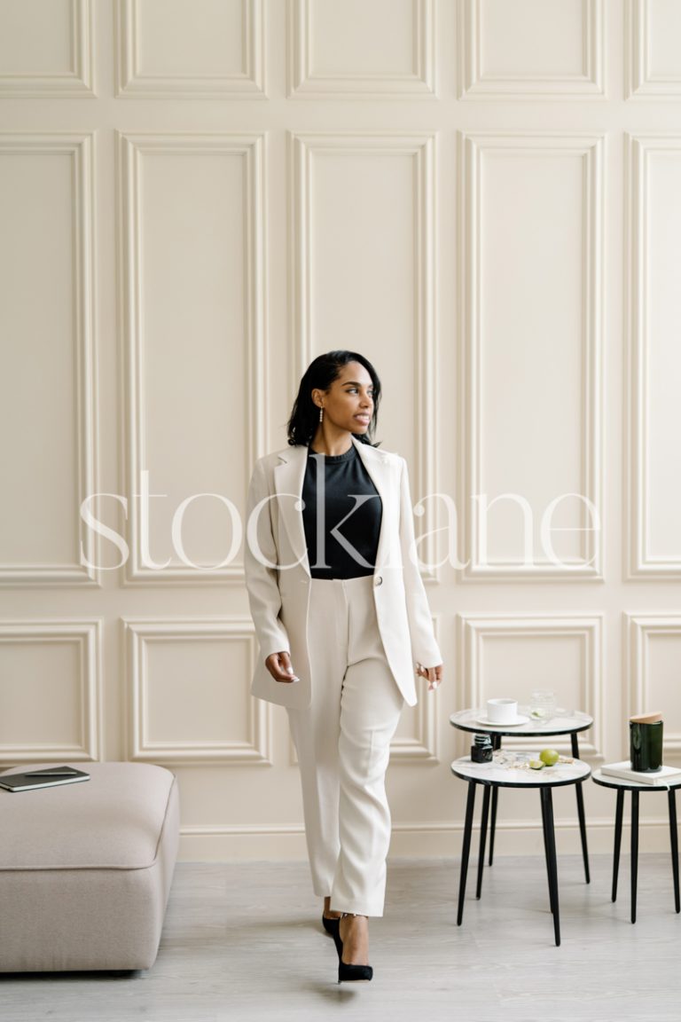 Vertical stock photo of a woman wearing a white suit, in a neutral-colored room.