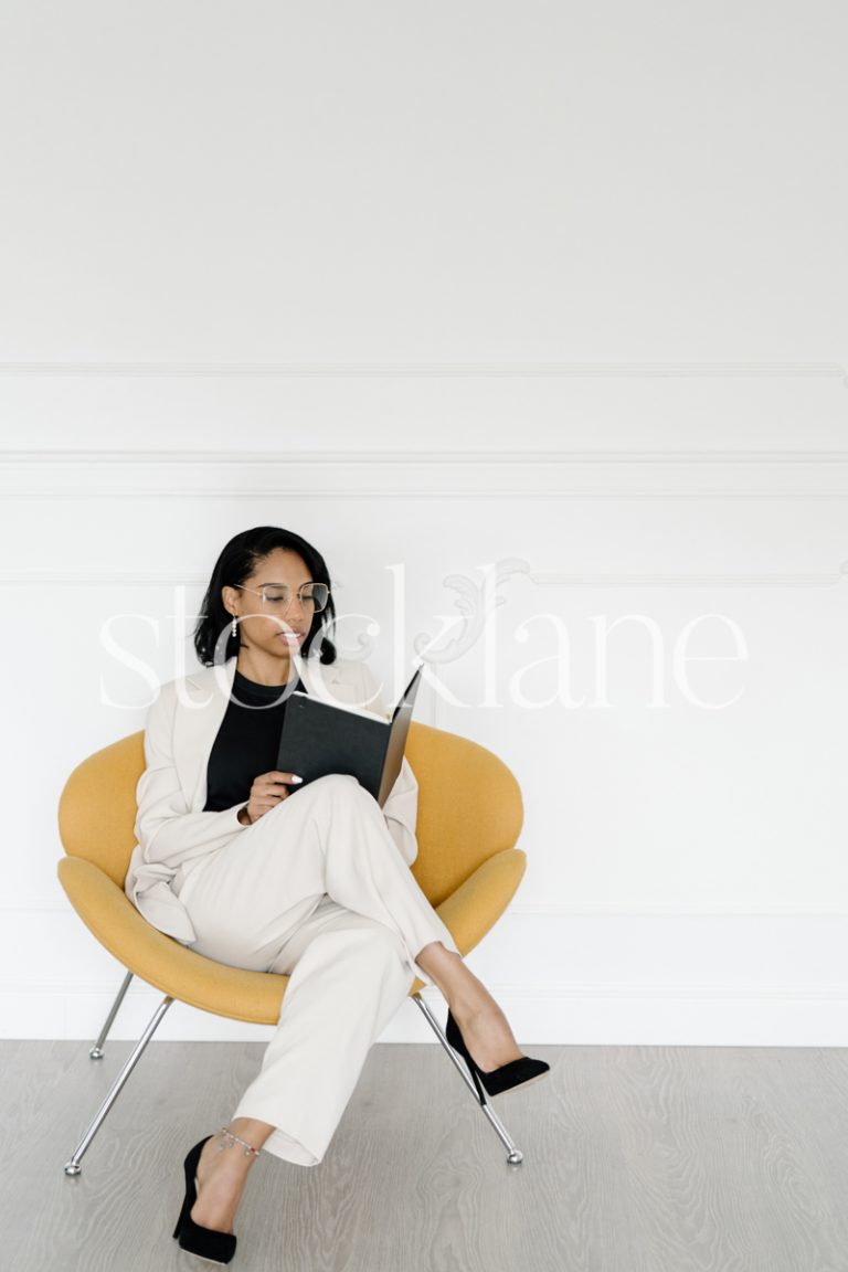 Vertical stock photo of a woman wearing a white suit, writing on a notebook.