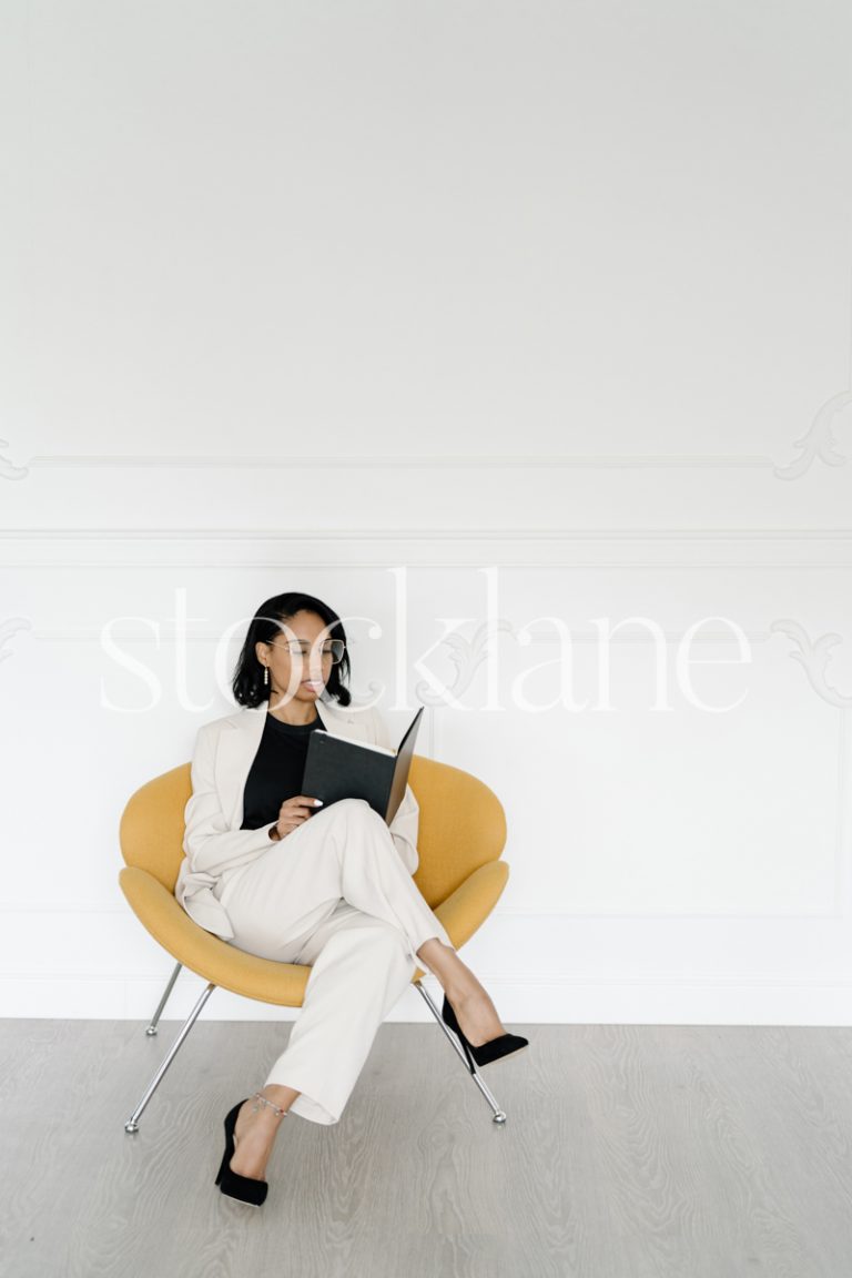 Vertical stock photo of a woman wearing a white suit, writing on a notebook.