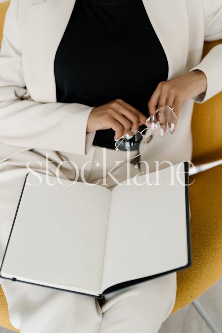 Vertical stock photo of a woman wearing a white suit, with a notebook.