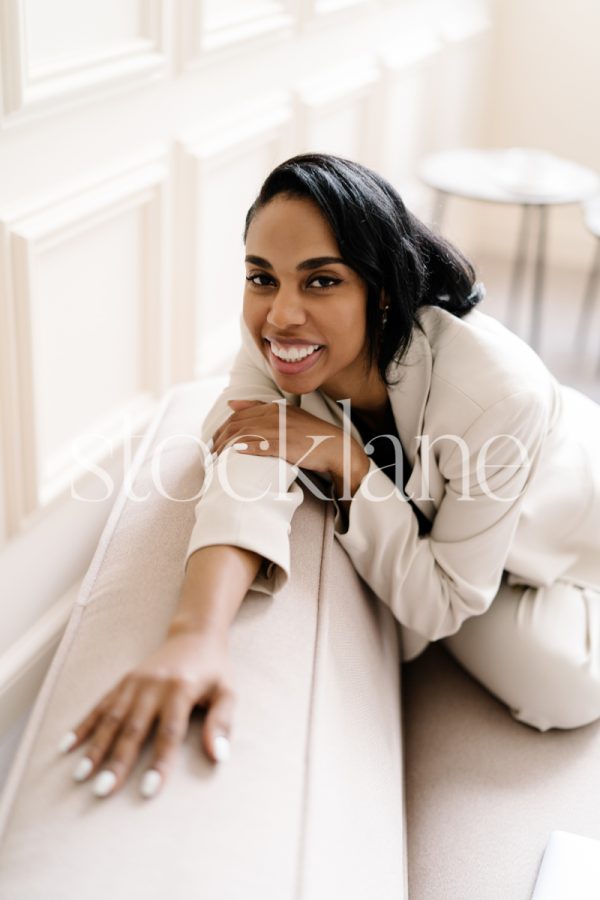 Vertical stock photo of a woman wearing a white suit sitting on a blush pink couch