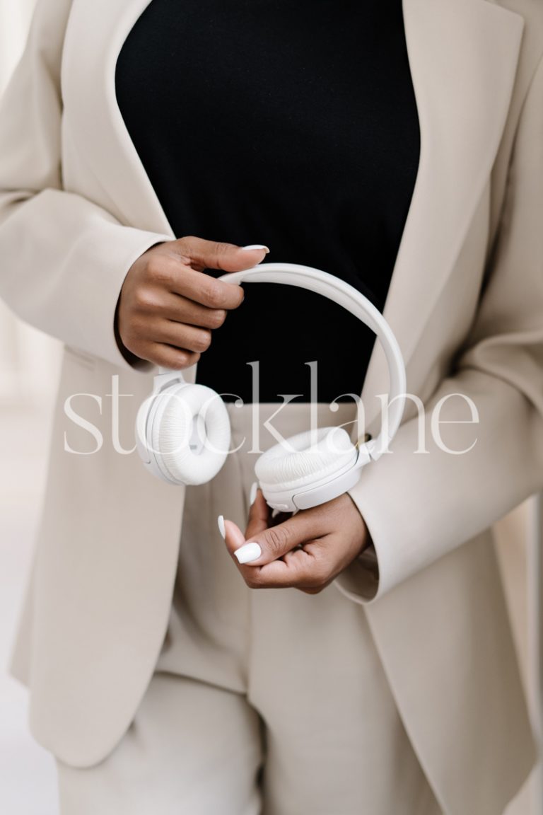 Vertical stock photo of a woman wearing a suit holding a pair of white headphones.