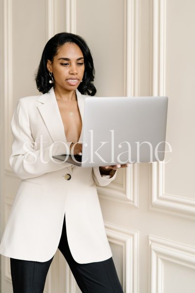 Vertical stock photo of a woman holding a computer, leaning against a wall.