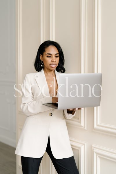 Vertical stock photo of a woman holding a computer, leaning against a wall.