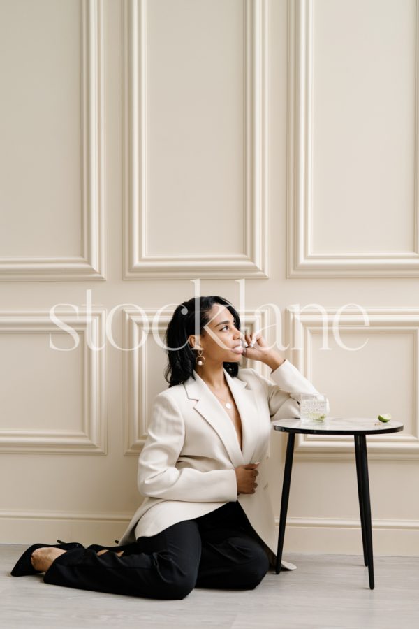 Vertical stock photo of a professional woman sitting on the floor, leaning on a table.