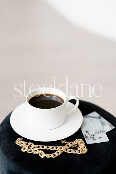 Vertical stock photo of a cup of coffee and jewelry on a table.