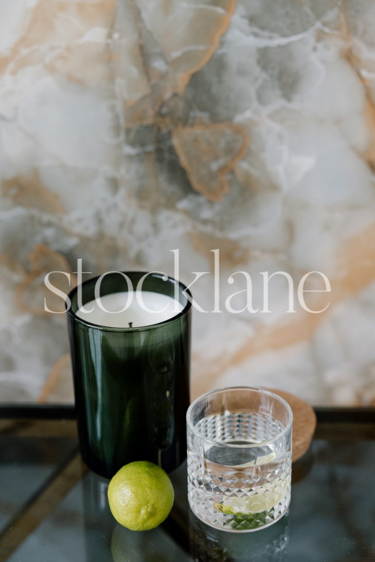 Vertical stock photo of a table with a candle, a glass of water and a lime.