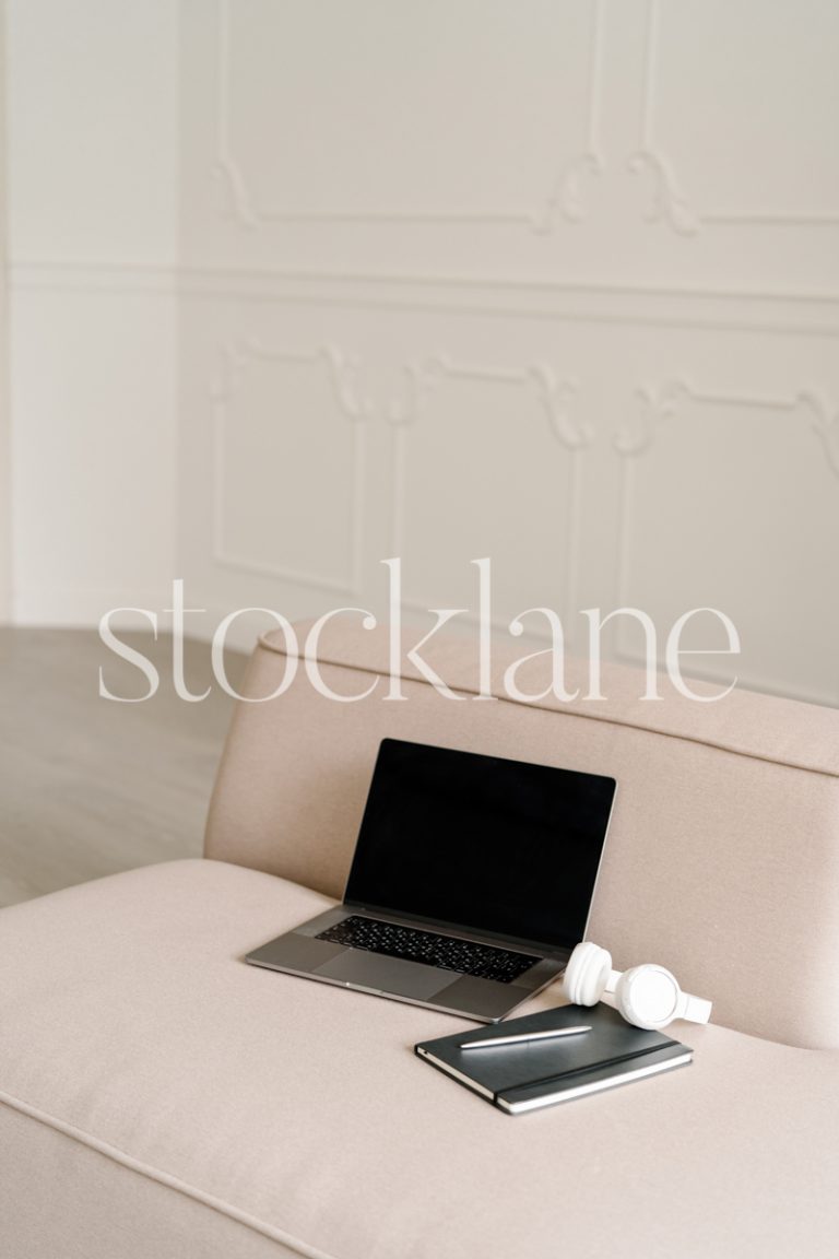 Vertical stock photo of a laptop computer and headphones on a blush pink couch.