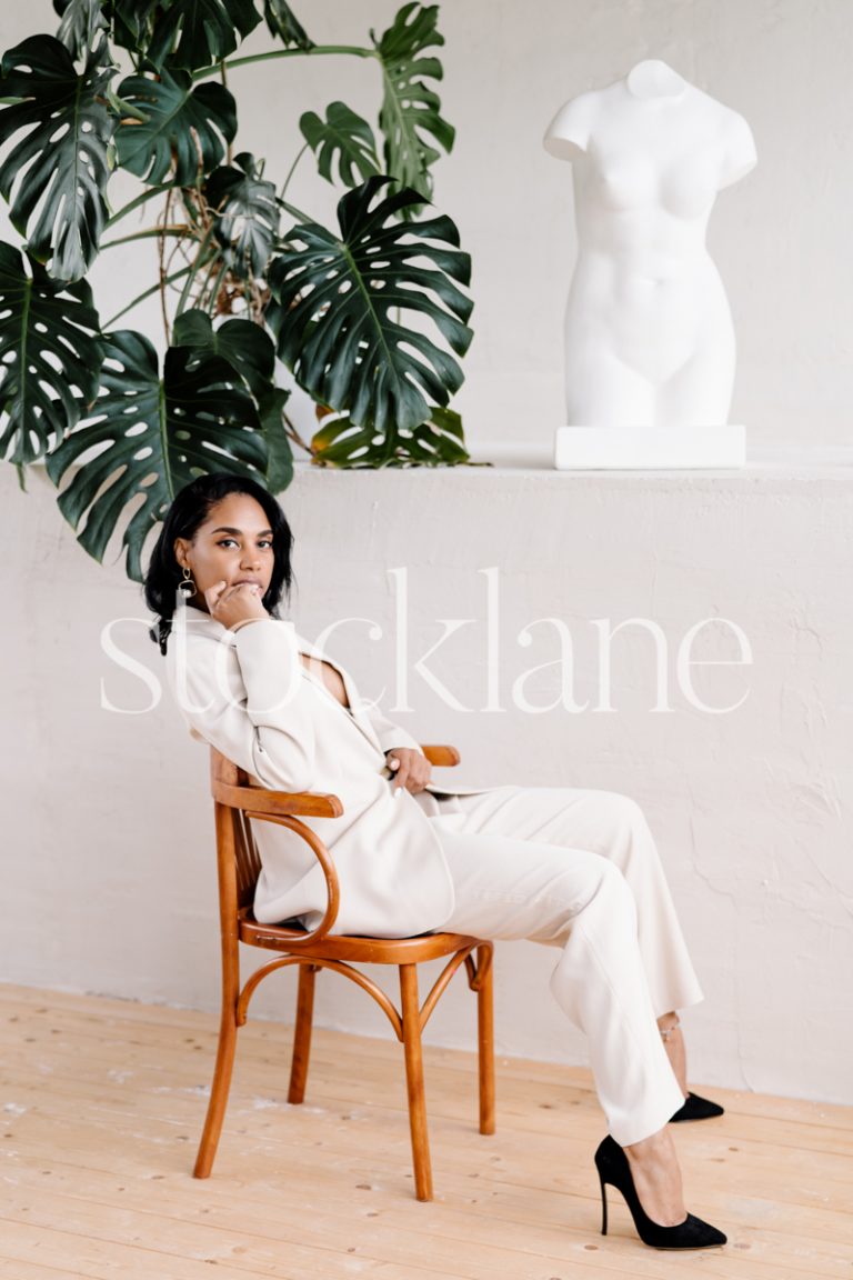 Vertical stock photo of a woman wearing a white suit sitting casually on a chair.