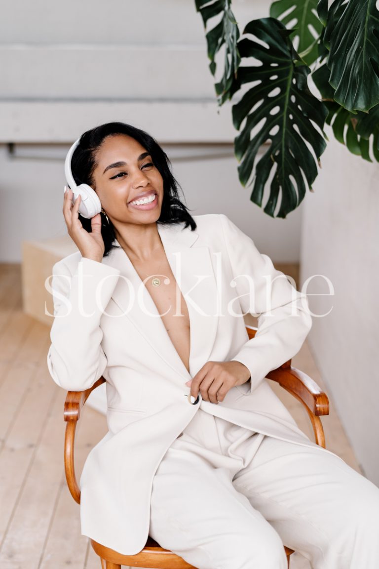 Vertical stock photo of a woman wearing a white suit and headphones.