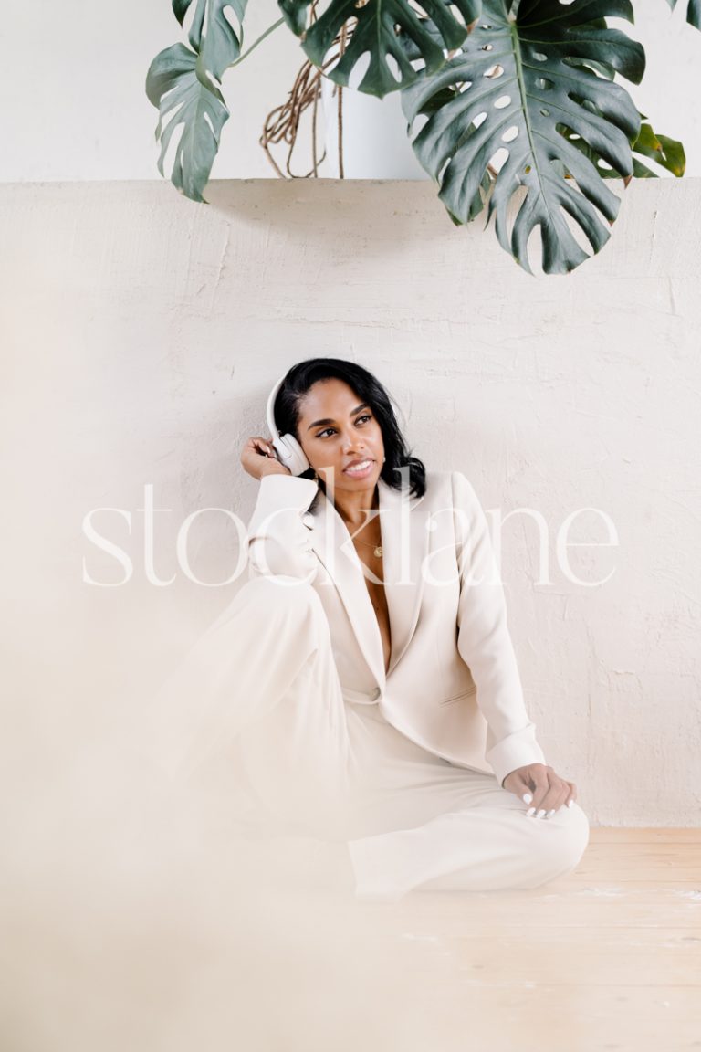 Vertical stock photo of a woman wearing a white suit, sitting on the floor.