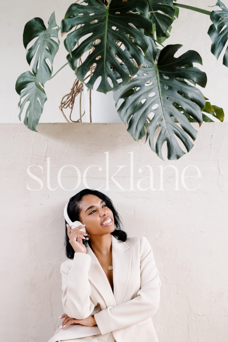 Vertical stock photo of a woman wearing a white suit, sitting on the floor, with headphones.