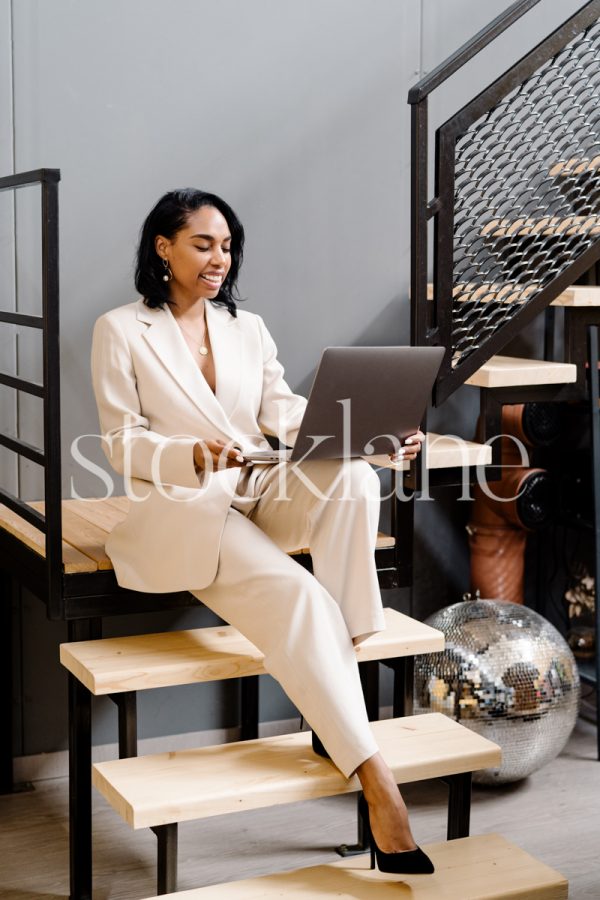 Vertical stock photo of a woman sitting on stairs, working on her laptop.