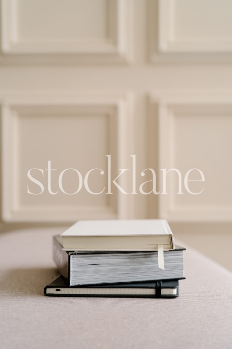 Vertical stock photo of a pile of books with a neutral wall background.