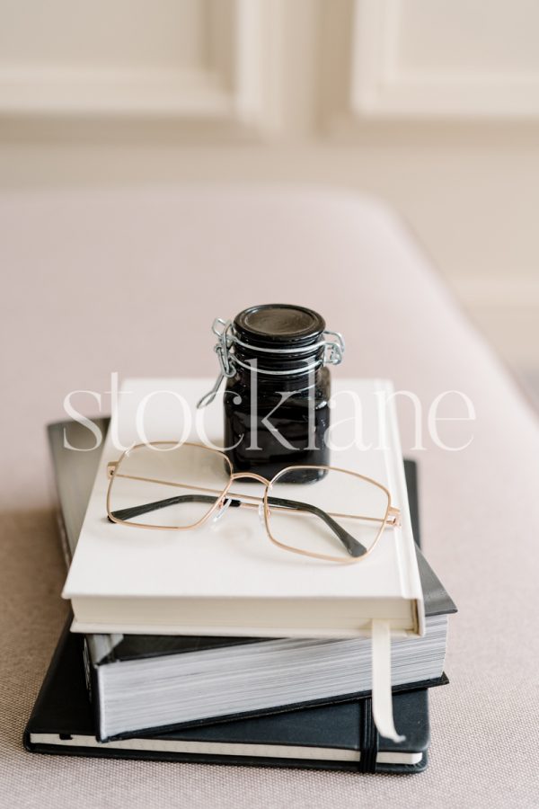 Vertical stock photo of a pile of books with a pair of glasses and a bottle of ink.