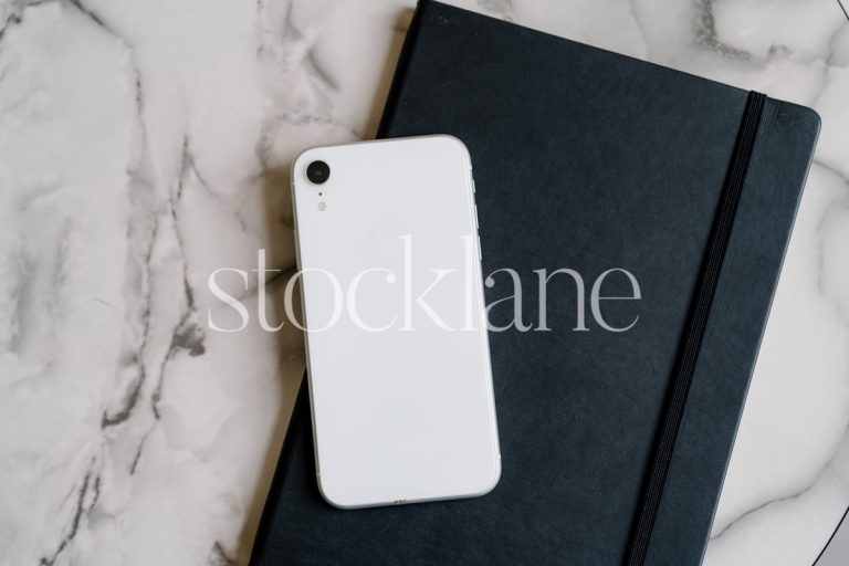 Horizontal stock photo of a black notebook and a phone on a marble background.