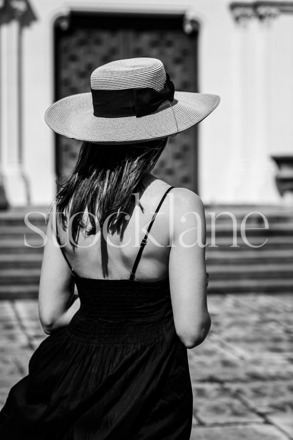 Vertical black and white photo of a woman wearing a black dress and a hat.